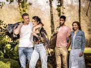Two young couples strolling with their arms around each other in a sunny park