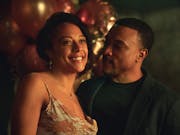 A Black woman in a cocktail dress and a Black man in a black suit at a party looking happy