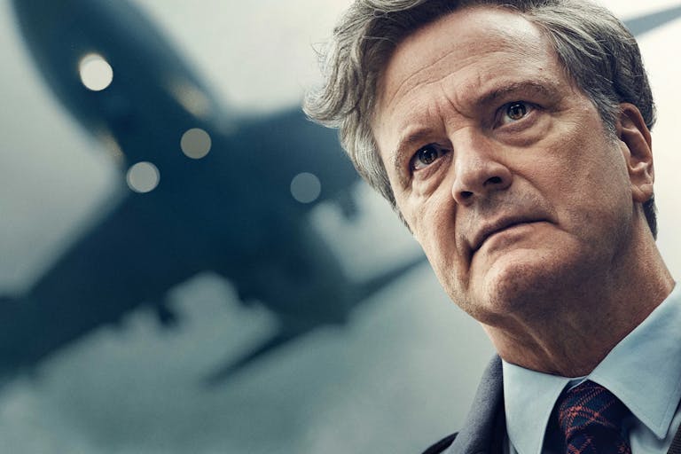 A middle aged white man with grey hair wearing a suit looking haunted as a plane flies overhead