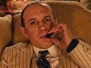 A middle aged white man in a white pinstripe suit smoking a cigar