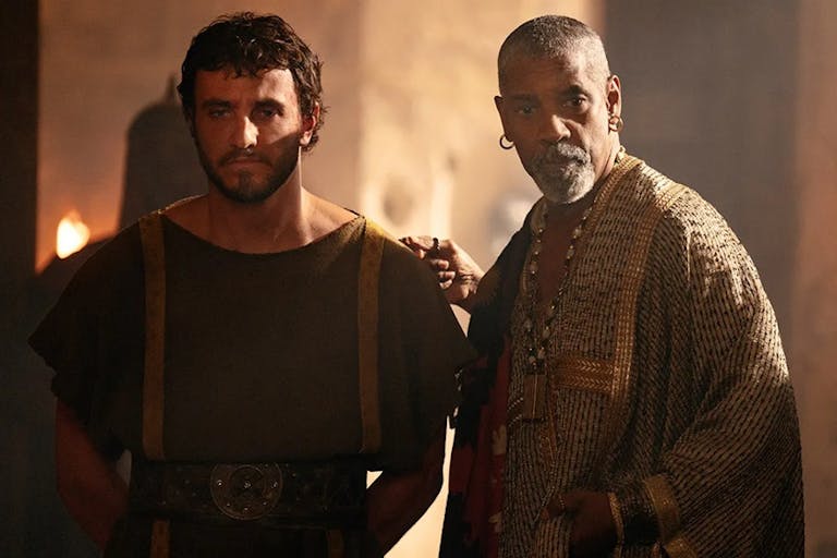 A young white man in plain robes with his hands behind his back stands besides a middle aged Black man in elegant robes
