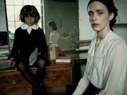 A woman in a white shirt and creepy child in a black and white 1800 school uniform are looking intensely at the camera