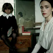 A woman in a white shirt and creepy child in a black and white 1800 school uniform are looking intensely at the camera