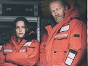 A white man and a white woman in thick orange jackets are looking