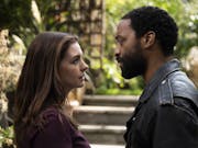 White woman and black man in a park are standing close to each other talking.
