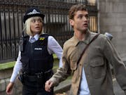 Man and woman (in police uniform) walk by a gated park and are surprised by looking at something on the right of the camera