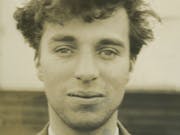 A black and white close up still of a young man with short wild hair, a slight smile on his face