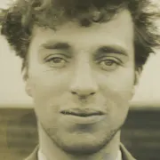 A black and white close up still of a young man with short wild hair, a slight smile on his face
