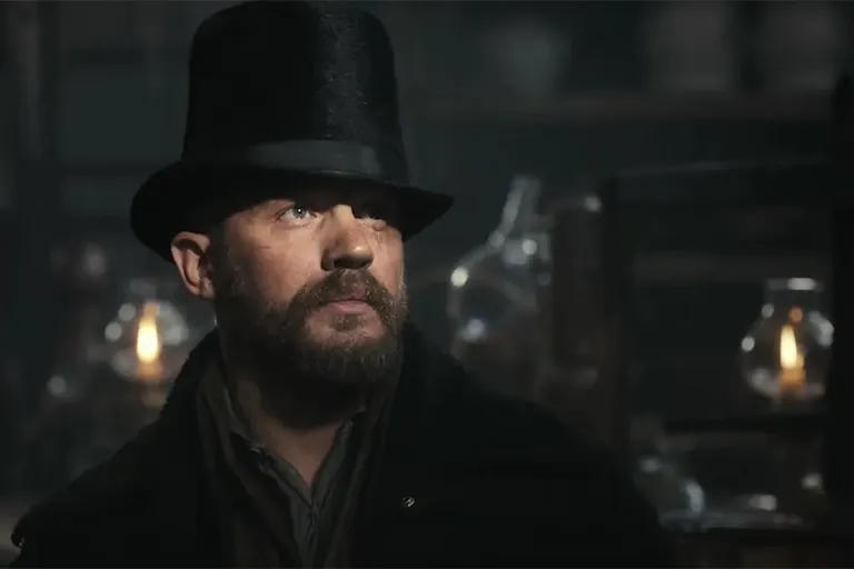 A white man with a rugged beard wearing a tall hat, gas lamps in the background