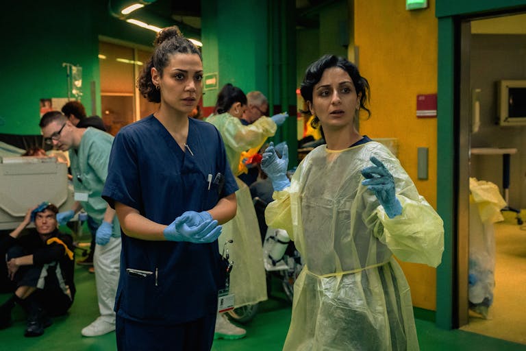 Two young in surgery scrubs in a busy ER setting