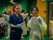 Two young in surgery scrubs in a busy ER setting
