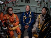 Three men in uniform sitting inside a submarine looking defeated