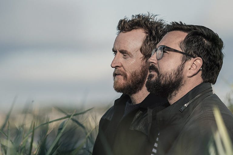 Side profile of two white bearded men standing in a long grass field