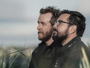 Side profile of two white bearded men standing in a long grass field