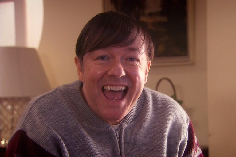 A white middle aged man with combover and grey cardigan smiling widely
