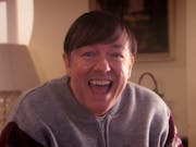 A white middle aged man with combover and grey cardigan smiling widely