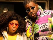 A young Black woman and man in colourful clothing and sunglasses looking seriously at the camera