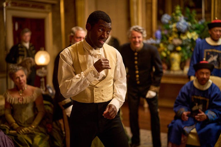 A young Black man in a Victorian suit in a fighting stance in a grand room with other Victorian people spectating