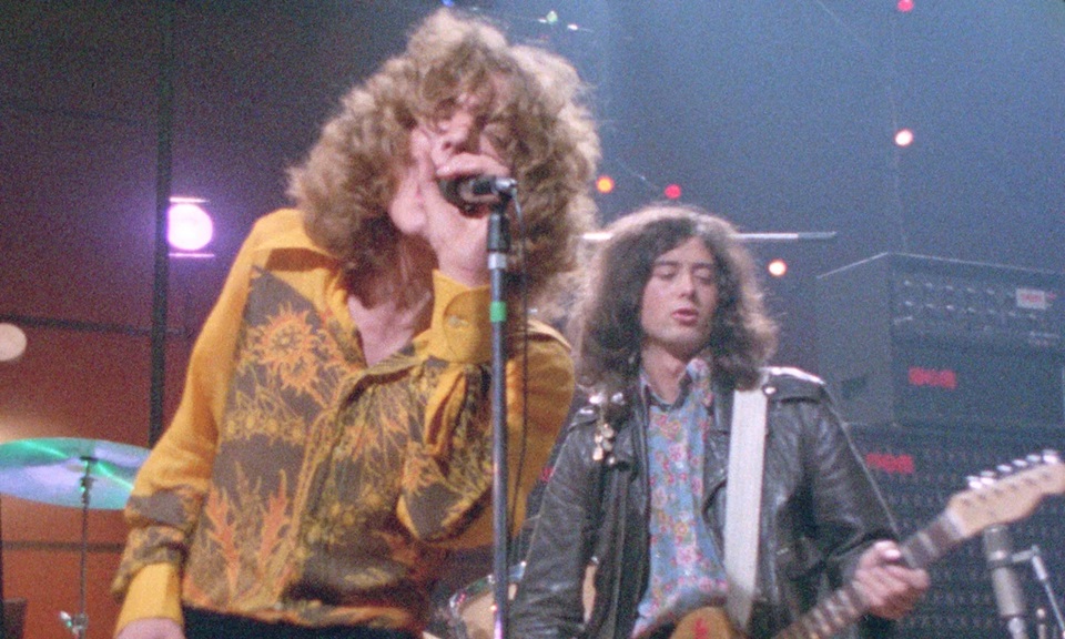 Two white men with big hair and 80s clothing on stage playing instruments