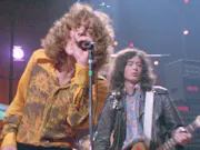Two white men with big hair and 80s clothing on stage playing instruments
