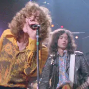 Two white men with big hair and 80s clothing on stage playing instruments