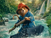 A CGI bear in blue coat and red hat, rafting on an open upturned umbrella down a river