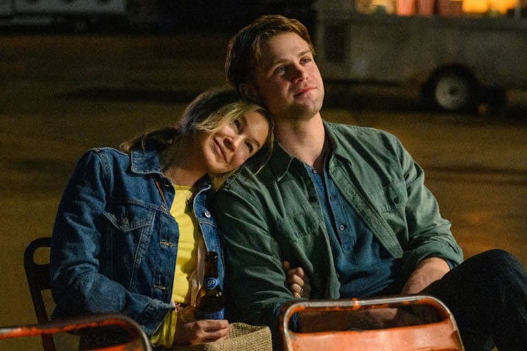 A white woman looking happy with her head resting on a young white man's shoulder