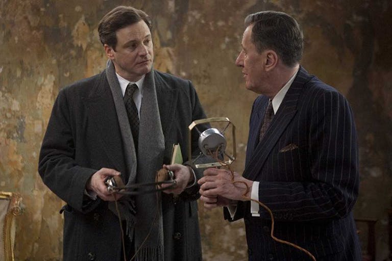 Two middle aged white man in smart suits holding an early 20th Century microphone