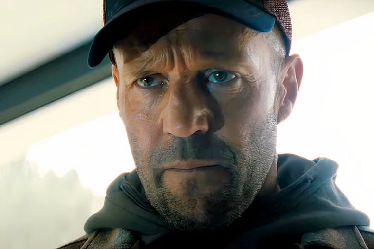 A close-up of actor Jason Statham, as the character Levon Cade, wearing a hoody and cap, staring intensely.