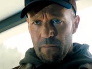 A close-up of actor Jason Statham, as the character Levon Cade, wearing a hoody and cap, staring intensely.