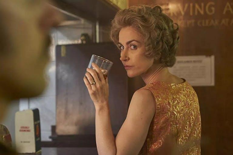 A white woman sits at a bar with a drink
