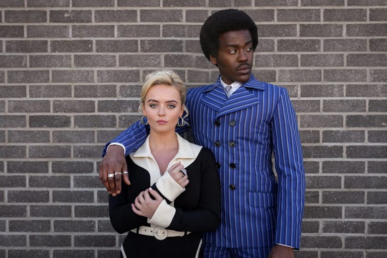 A young white woman and a young Black man in 60s fashionable clothing and hairstyle, his arm around her