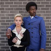 A young white woman and a young Black man in 60s fashionable clothing and hairstyle, his arm around her