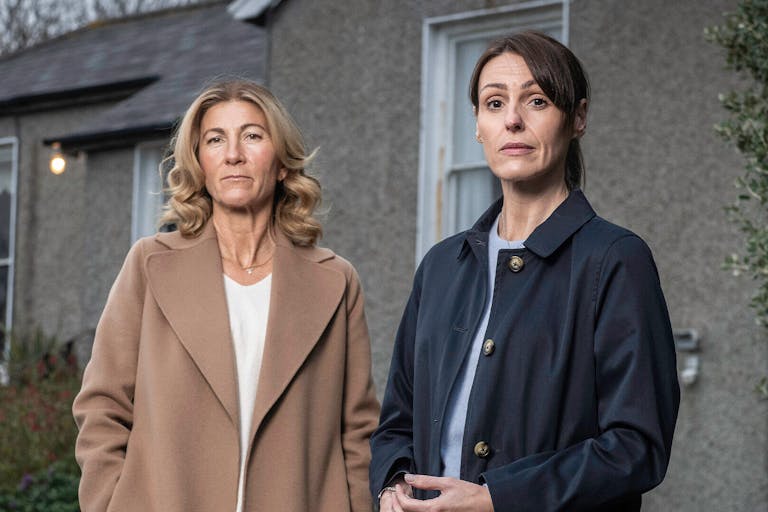 Two white women looking serious in front of a house