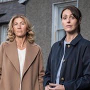 Two white women looking serious in front of a house