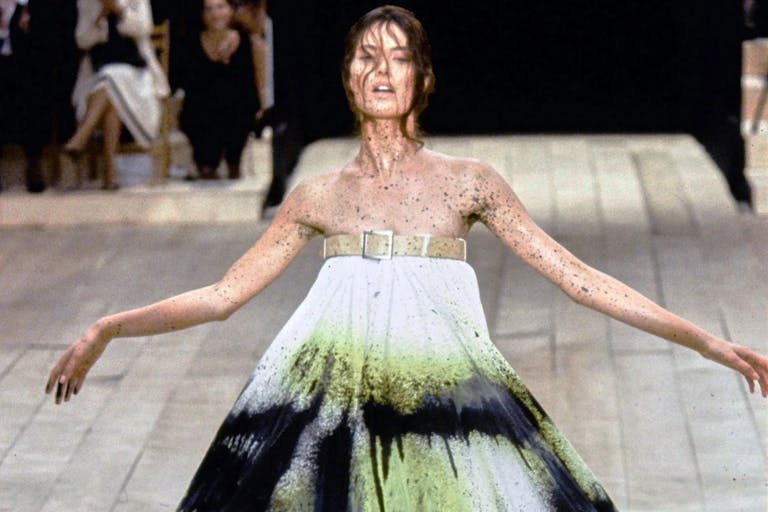 A woman model in an Alexander McQueen dress with belt at the top, sprayed with black and neon green paint