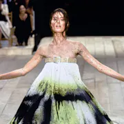 A woman model in an Alexander McQueen dress with belt at the top, sprayed with black and neon green paint