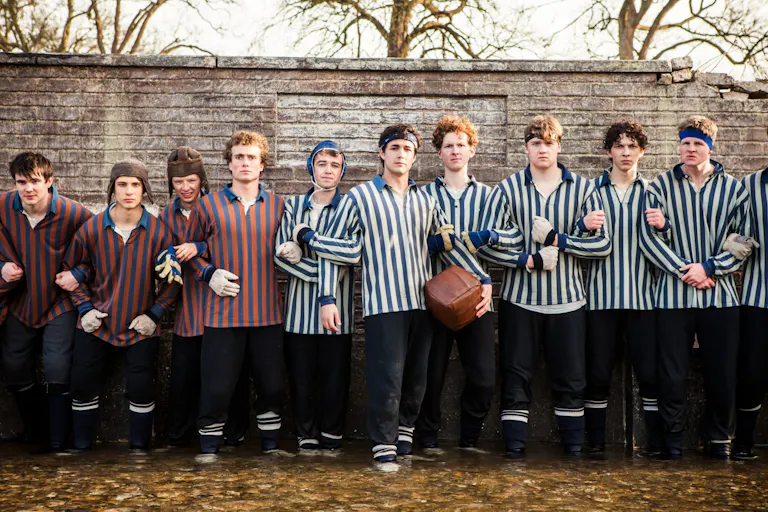 A long line of young teen boys in striped 80s boarding school football uniforms linking arms