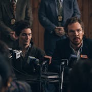 A white woman and white man looking tired speaking at a press conference with police detectives standing behind them