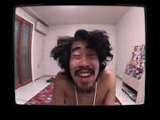 A Japanese man with wild dark hair in a room, staring manically at the camera, framed by a TV screen