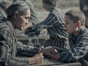 A white man and white woman with shaved heads in striped concentration camp clothing looking across as each other