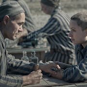 A white man and white woman with shaved heads in striped concentration camp clothing looking across as each other