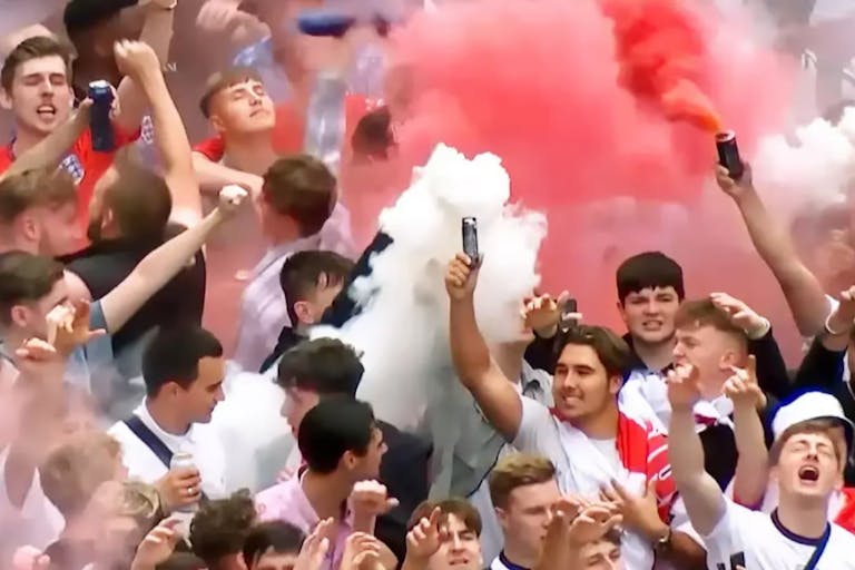 A group of majority young white men in England supporter football shirts letting off red and white flares