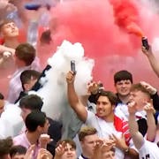 A group of majority young white men in England supporter football shirts letting off red and white flares