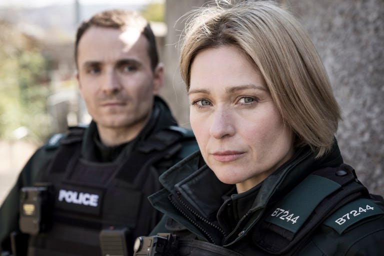 A white man and woman in black police uniforms looking serious