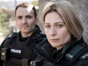A white man and woman in black police uniforms looking serious