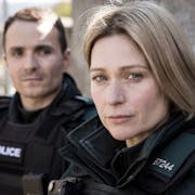 A white man and woman in black police uniforms looking serious
