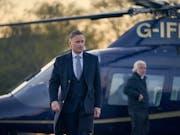 A white man in a suit walking away from a landed helicopter
