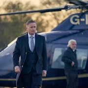 A white man in a suit walking away from a landed helicopter
