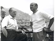Black and white photograph of two older men looking off into the distance with a coast view behind them